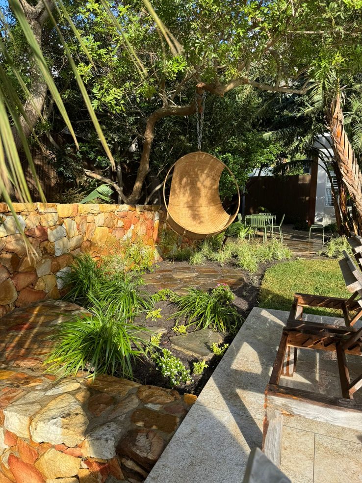 Finished courtyard by Element Landscapes — natural stone wall, hanging chair and layered planting