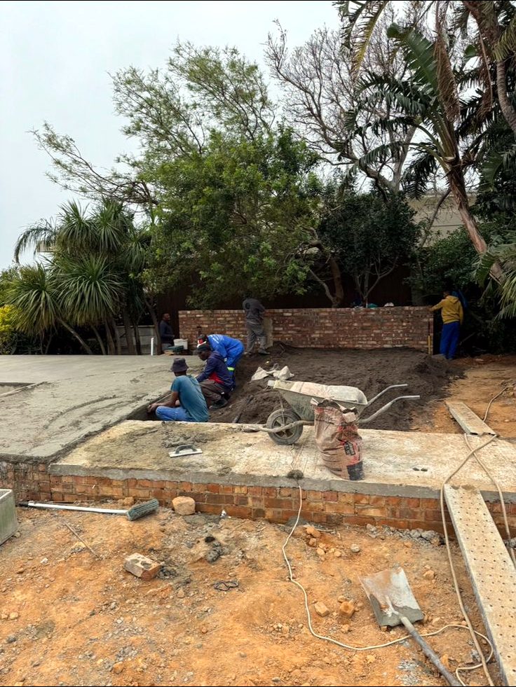 Construction site with exposed brickwork, bare earth and builders at work on a raised garden wall