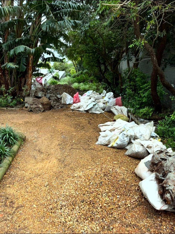 Dirt path beneath large trees lined with bags of building rubble during construction