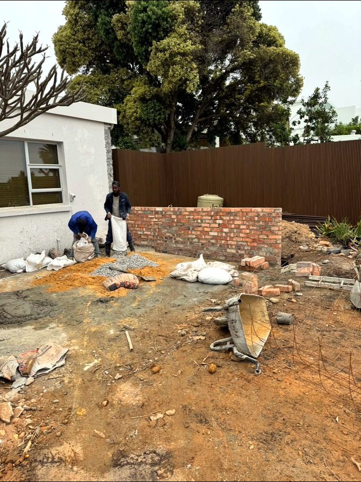 Bare corner of the property with building rubble, a half-built brick wall and exposed soil