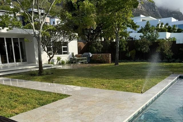 Irrigation sprinkler watering a newly laid lawn beside a travertine walkway