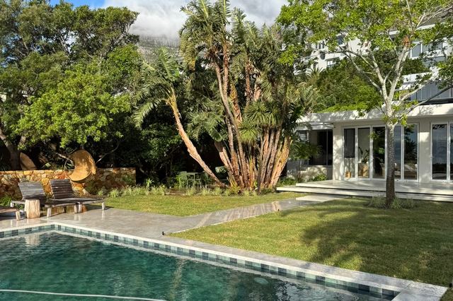 Lush level lawn beside a pool with a sculptural tree and the house behind
