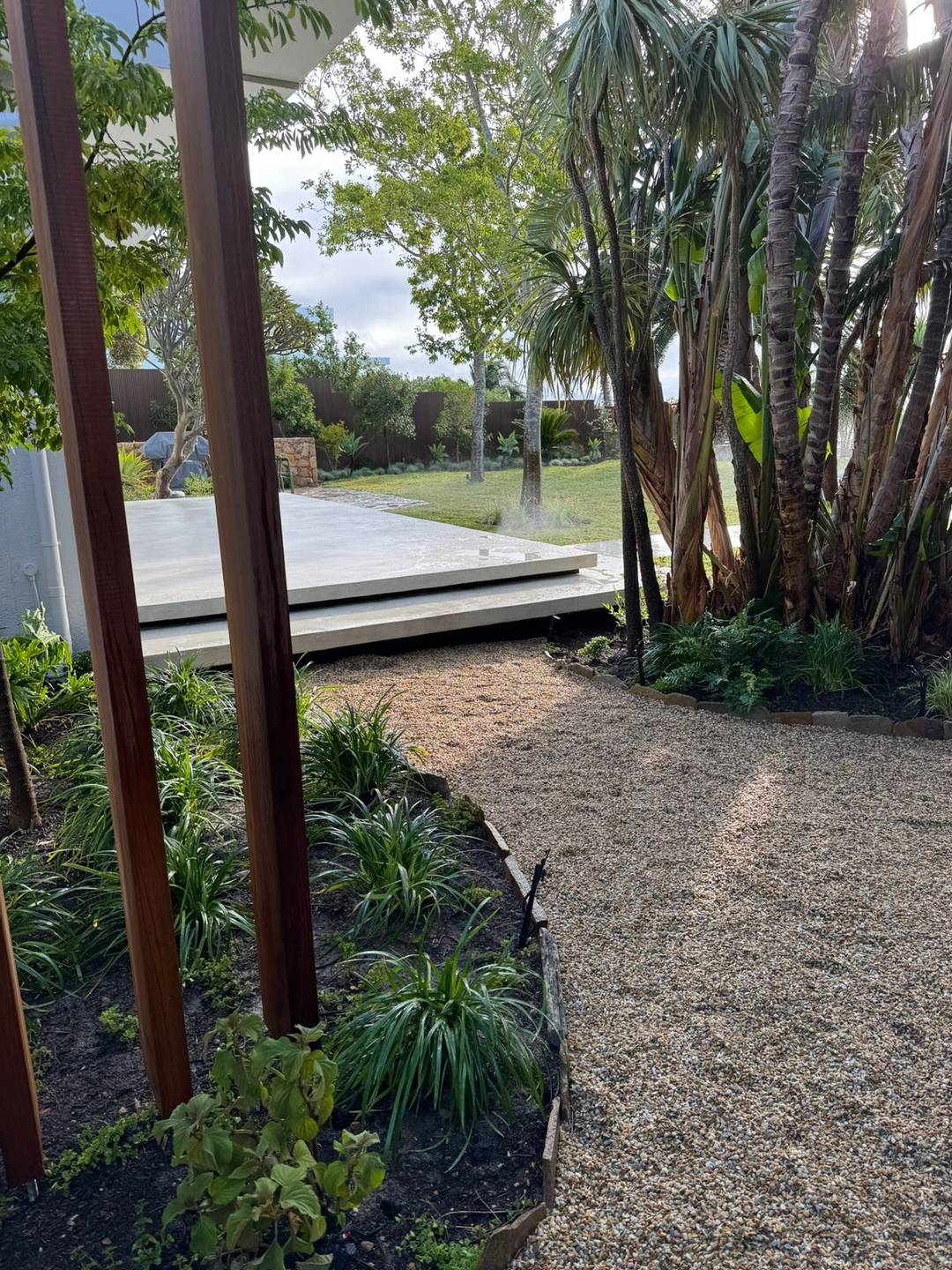 Weathered corten steel columns rising from a gravel bed planted with agapanthus
